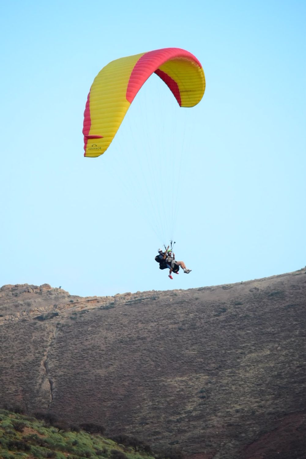 Tandem sous une voile jaune et rouge au-dessus de la crête